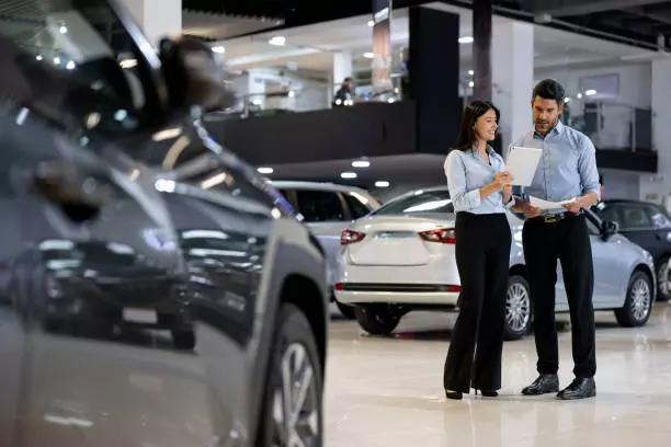 salespersons working together at a car showroom and reading a contract on a tablet